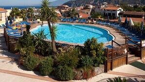 A pool surrounded by blue lounge chairs and palm trees, with buildings and a mountain in the background. - Grand Hotel La Pace (Sant'Agnello)