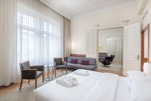 Camera d'albergo con un letto grande, un divano grigio, un tavolino e una sedia.