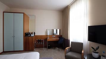 A hotel room with a bed, a desk, a chair, a TV, and a wardrobe.