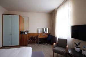 Una habitación de hotel con cama, escritorio, silla, televisor y armario.