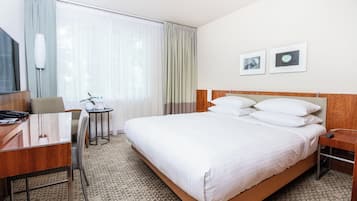 Ett hotellrum med en stor säng, ett skrivbord med en telefon, en stol, ett litet bord med en växt och en tv.