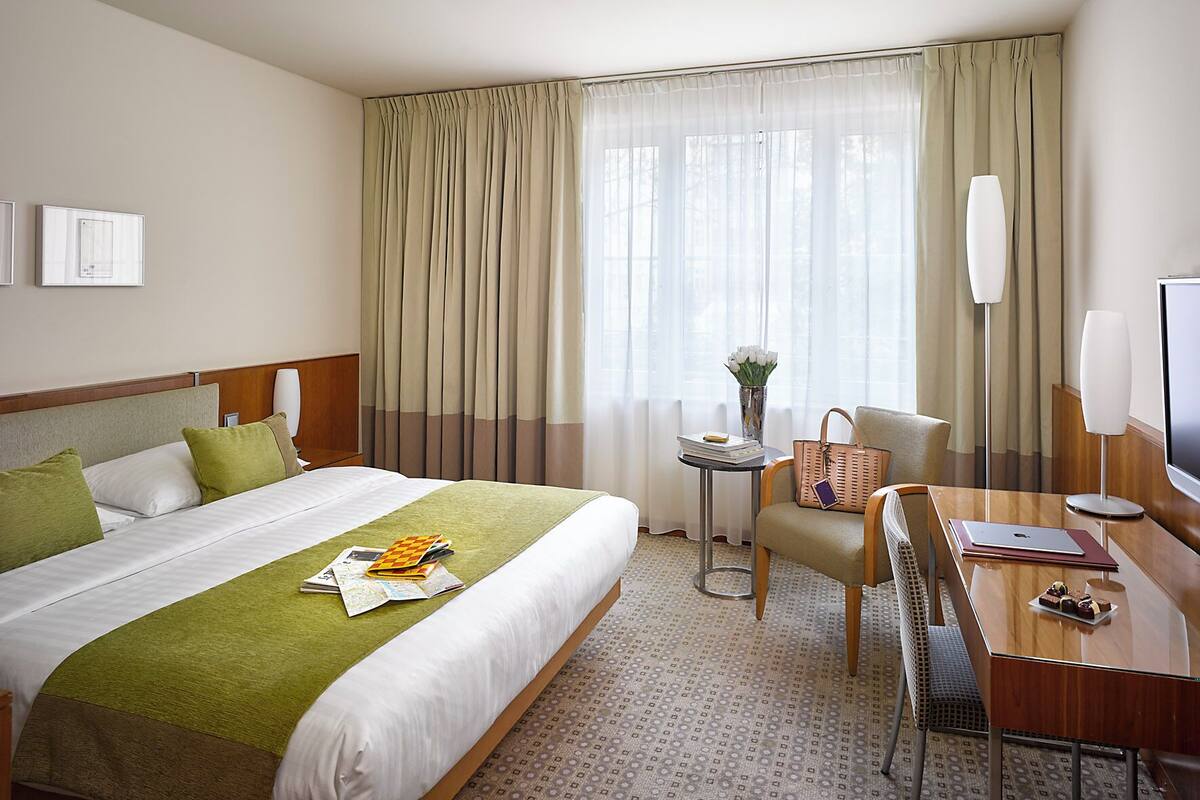 A hotel room with a bed, a desk, a chair, a TV, and a window with curtains.
