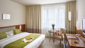 Habitación de hotel con cama, escritorio, silla, televisor y ventana con cortinas.