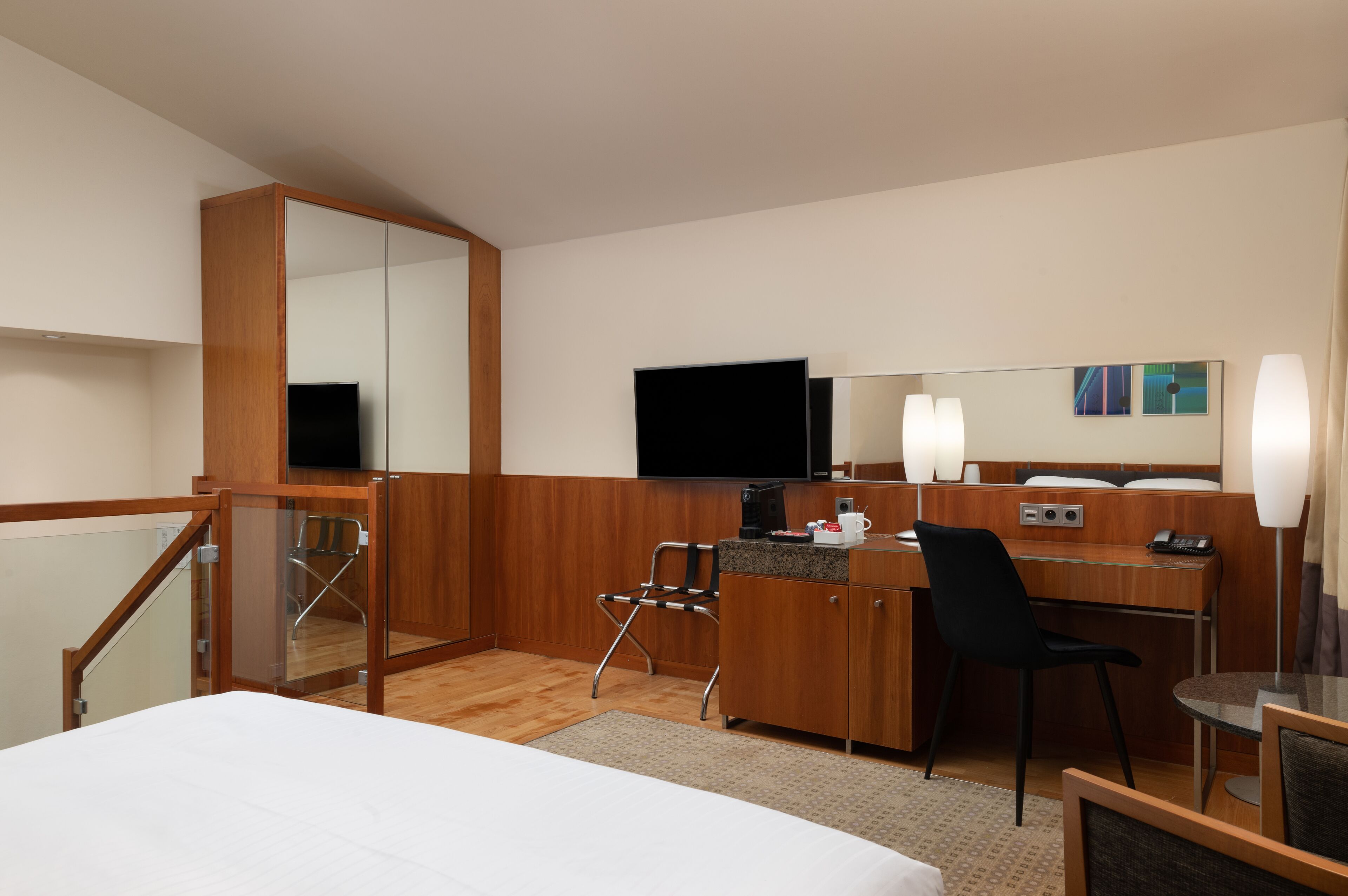A hotel room with a bed, desk, chair, television, and a large mirror.