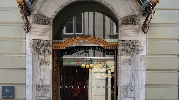Una entrada ornamentada con un arco negro, dos plantas en macetas y un cartel que dice "KK Hotel Central".