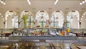 Amplia zona de desayuno con servicio tipo buffet, que incluye diversas opciones de comida y bebidas, en una sala con techos abovedados y ventanas amplias.