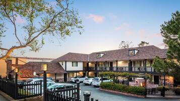 Un hotel con estacionamiento cercado, varias habitaciones y un cartel que indica disponibilidad.