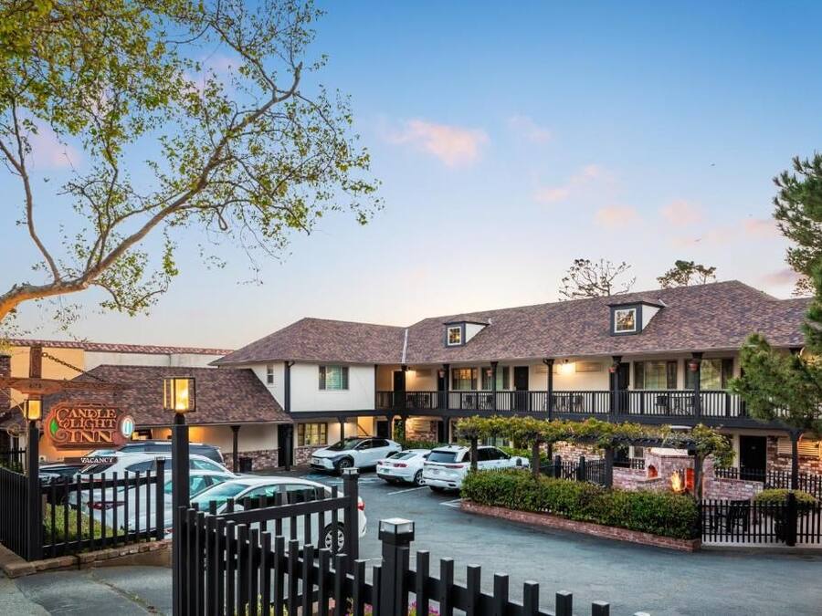Un hotel con estacionamiento cercado, varias habitaciones y un cartel que indica disponibilidad.