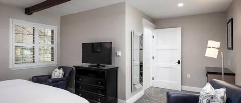 A bedroom with a bed, a dresser, a TV, a chair, a lamp, and a door.