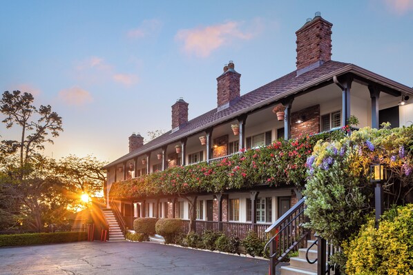 A two-story building with a brick facade, multiple chimneys, and a balcony with flowering plants. - Candle Light Inn (Carmel)