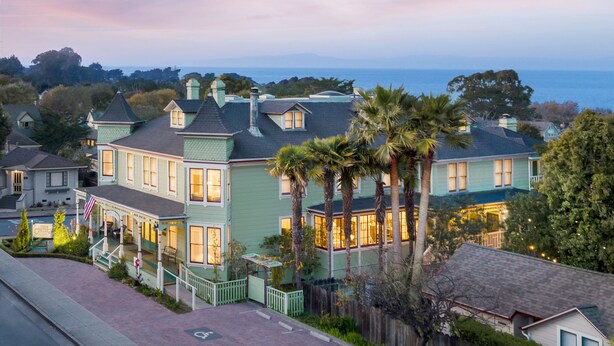 Una casa grande de estilo victoriano en verde claro, con varios pisos, un porche y vista al océano.