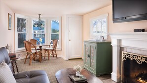 Una sala de estar con chimenea, un comedor con sillas, un televisor sobre la chimenea y vistas a través de las ventanas.