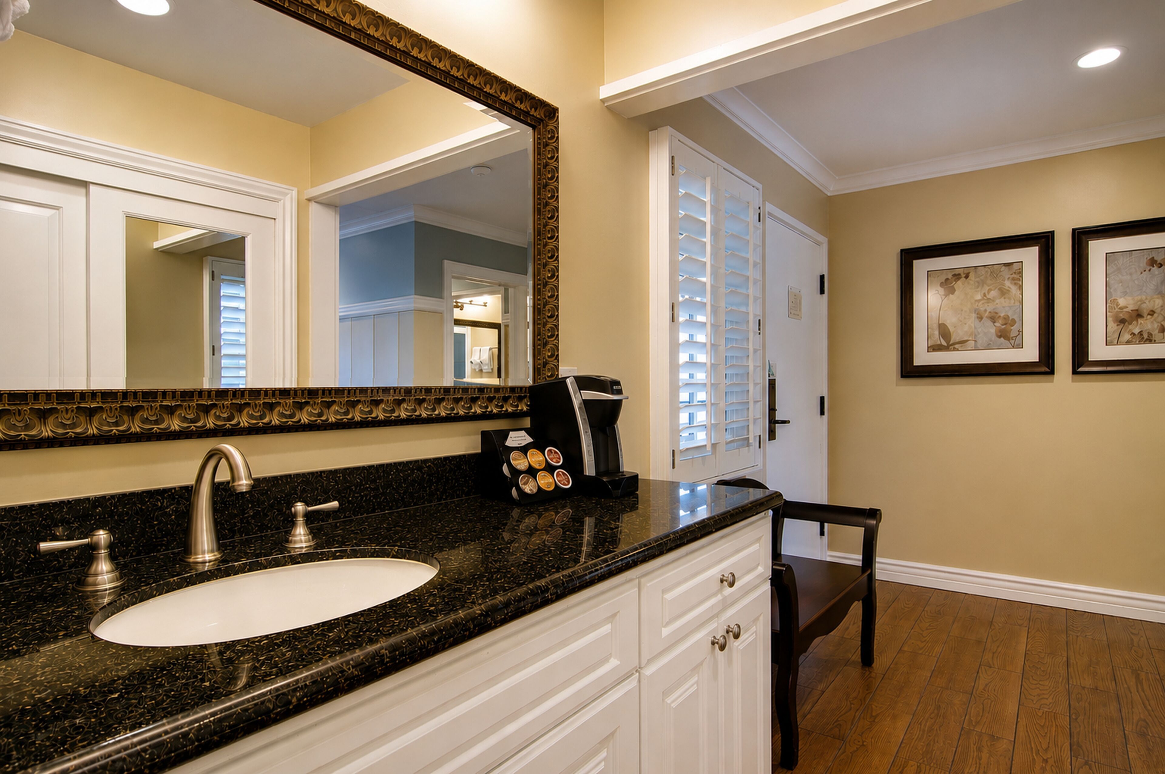 A bathroom with a large mirror, a sink, a coffee maker, and a chair.