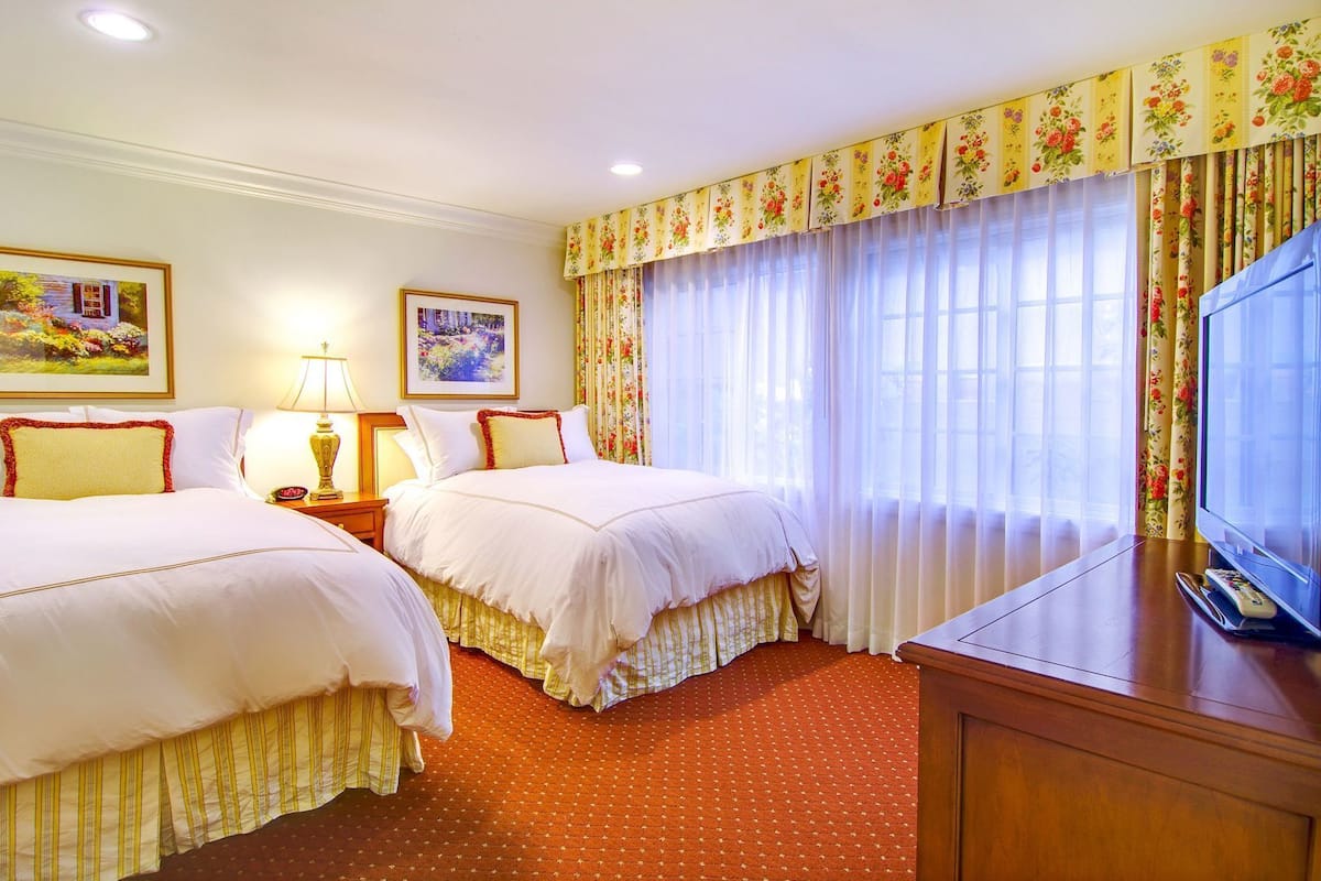 Quarto de hotel com duas camas, uma televisão, um abajur e um quadro na parede.