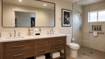 A modern bathroom with a large mirror, dual sinks, a shower enclosure, and a toilet.