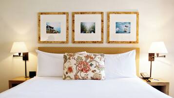 A hotel room with a bed, two nightstands, three framed pictures on the wall, and a floral pillow.