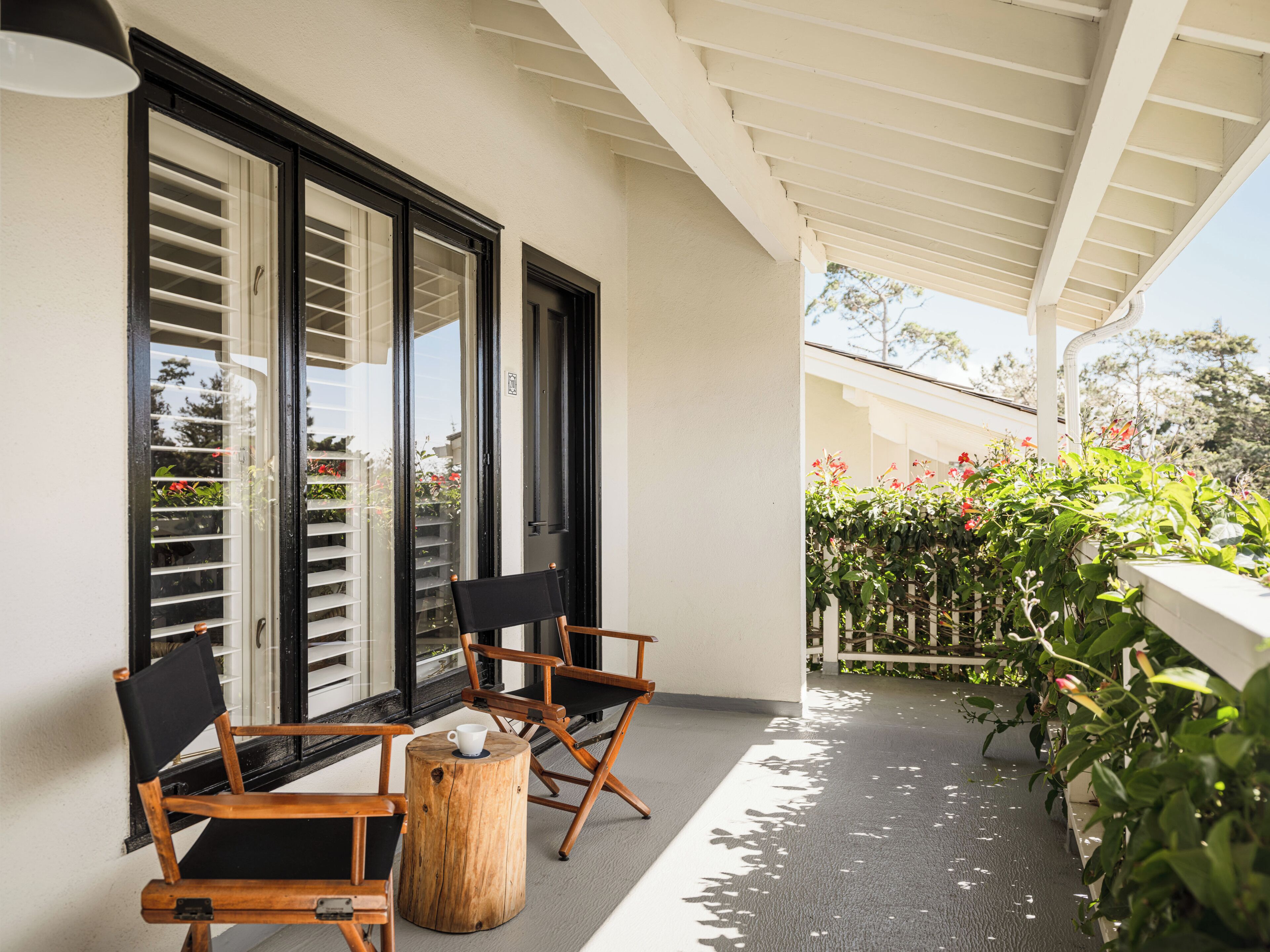 A balcony with wooden chairs, a round wooden stool, and a white cup on it.