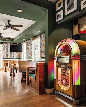 A retro-themed bar area with jukeboxes, wooden booths, and a green wall with framed pictures. - Hotel Carmel (Carmel)