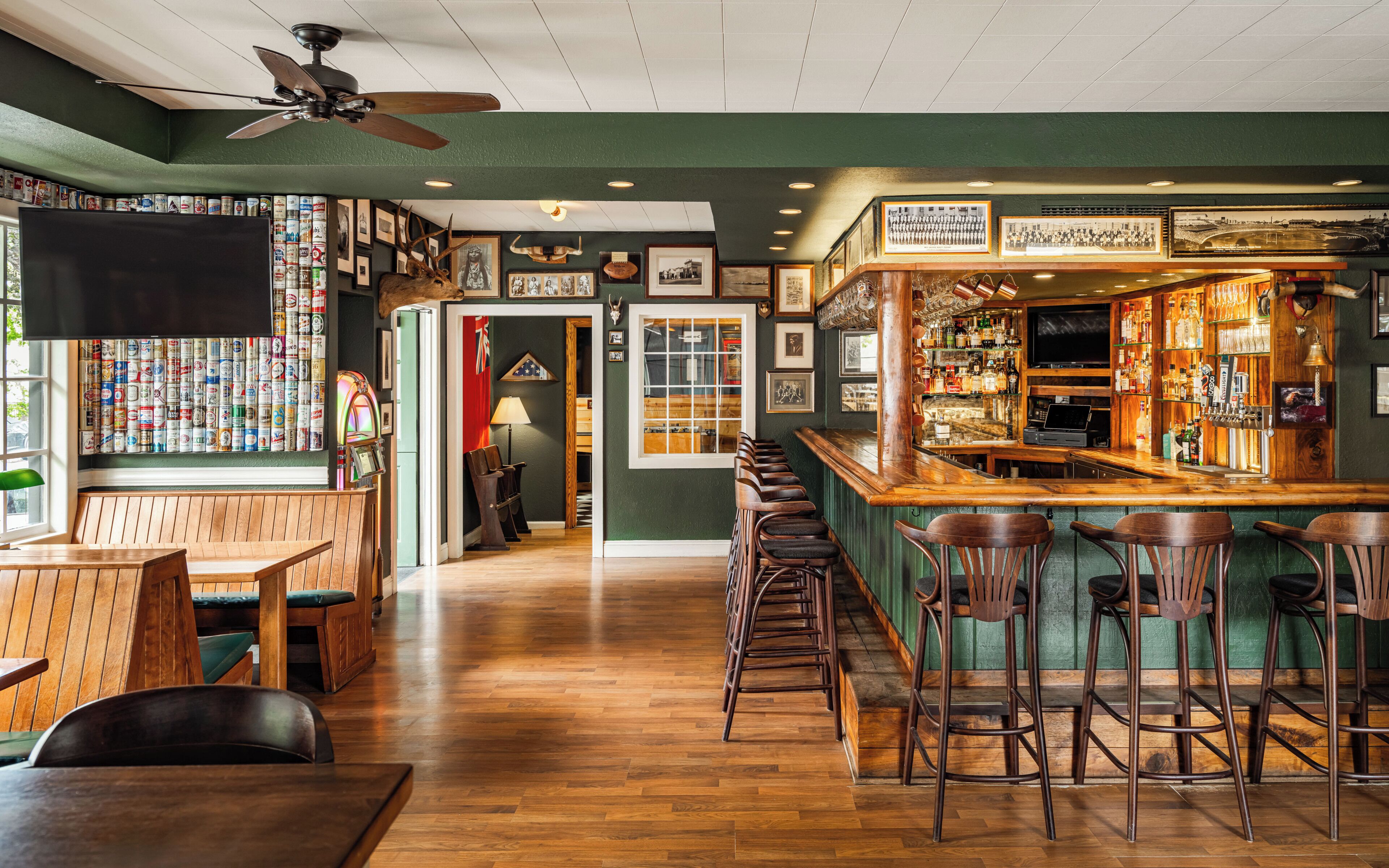 A bar area with wooden furniture, a counter with a cash register, and a wall with framed pictures and a shelf of bottles.