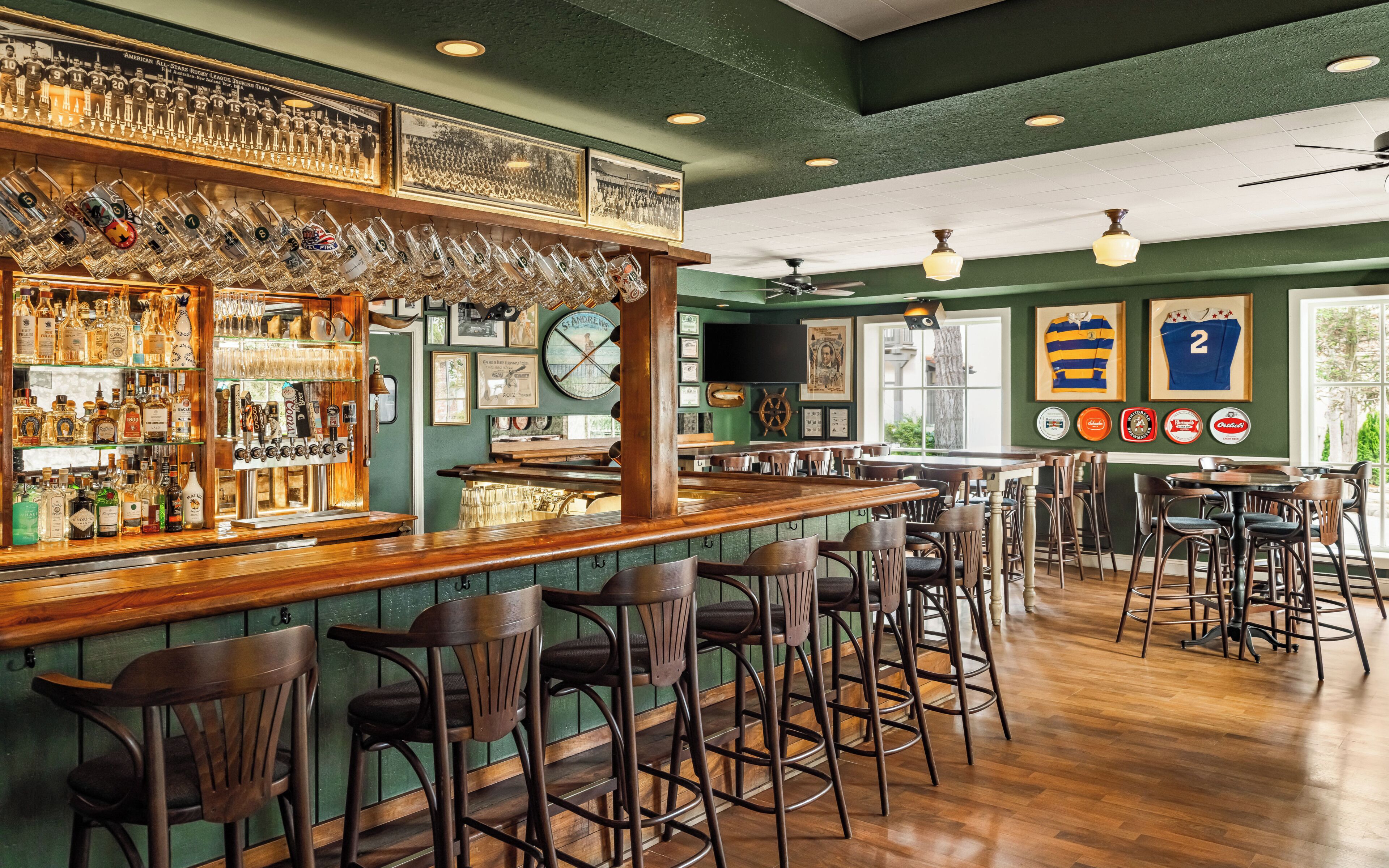 A bar area with wooden bar top, stools, and various bottles.