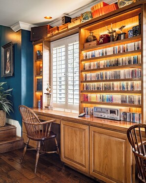A library with wooden bookshelves, a window with blinds, and a desk with a computer.