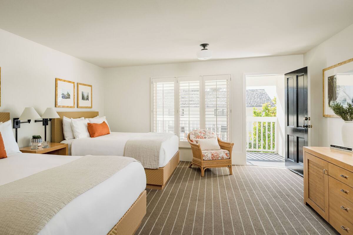 Une chambre d’hôtel avec deux lits, une chaise, un bureau et un balcon avec vue.