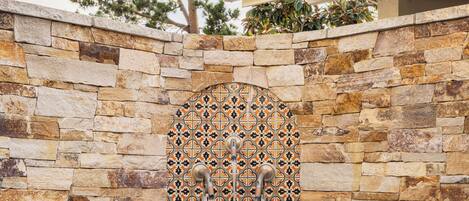 A stone wall with a decorative arch and a pool with water flowing from it.