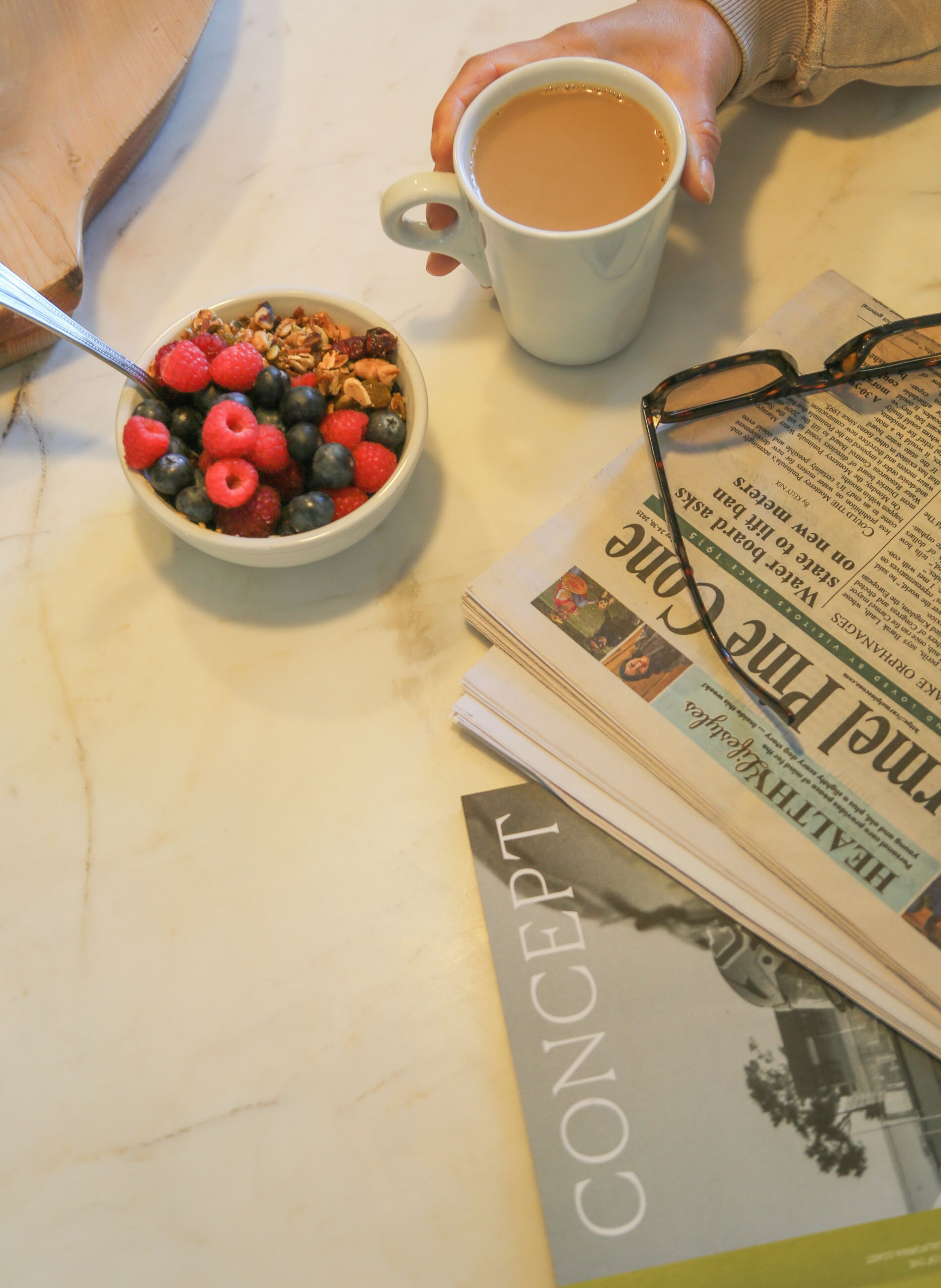 Un bol de céréales aux fruits rouges, une tasse de café et un journal sur une table.
