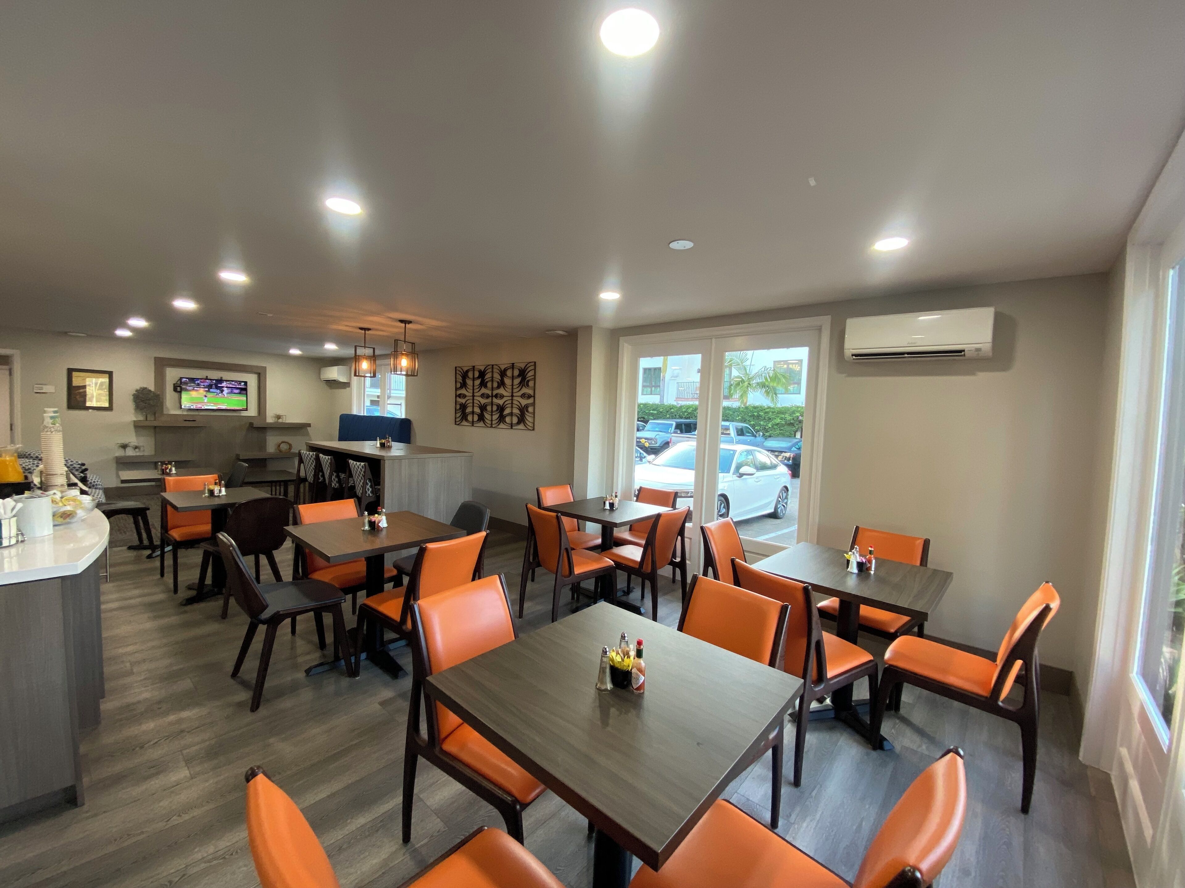 Ein Restaurant mit Holztischen und orangefarbenen Stühlen, einem Fernseher an der Wand und Blick auf geparkte Autos.