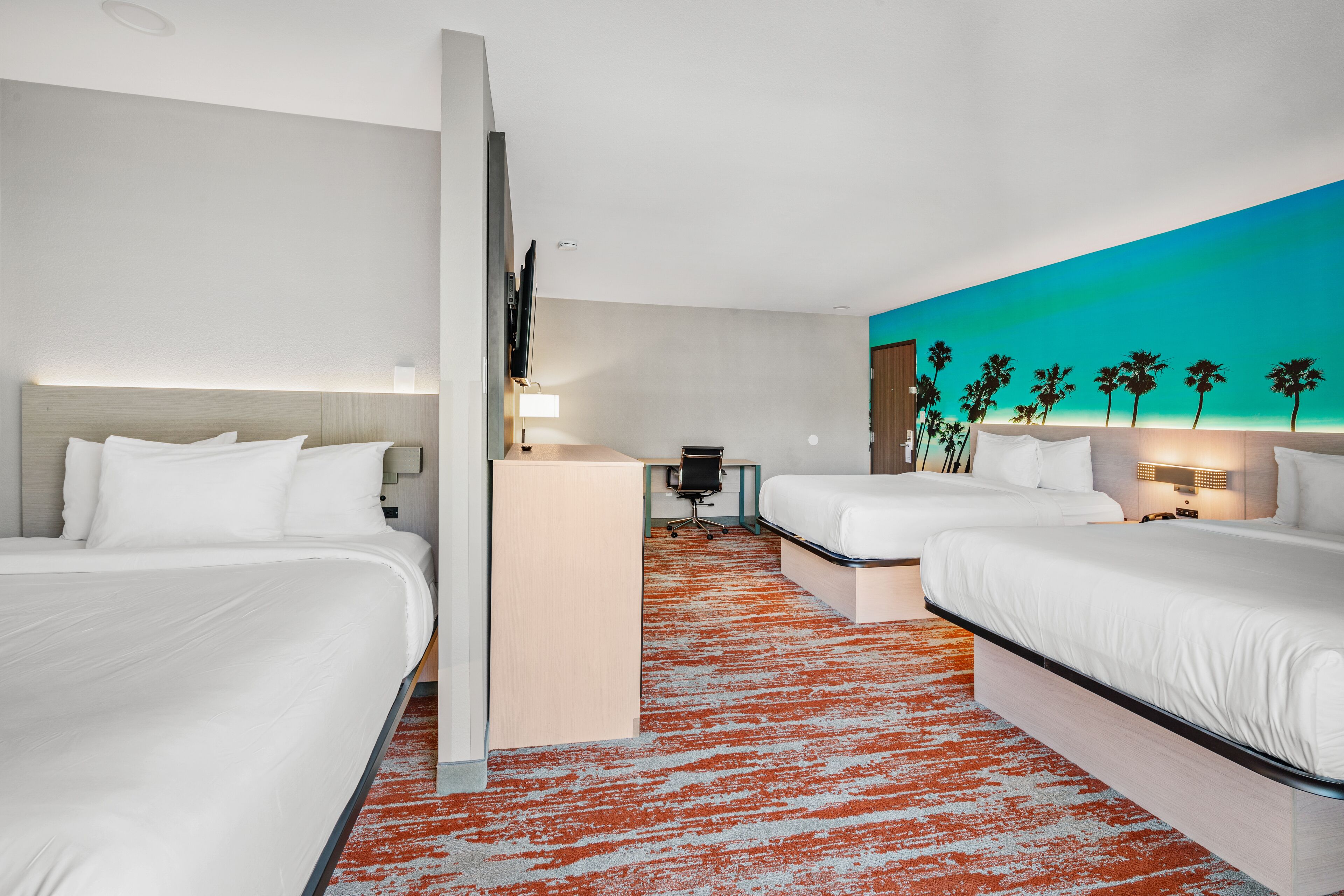 A hotel room with two beds, a desk, and a TV.