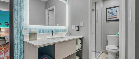 A modern bathroom with a large mirror, a sink, and a toilet. There is a towel rack and a trash bin.