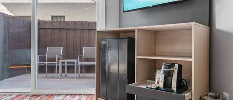 A room with a sliding glass door leading to an outdoor area, a black refrigerator, a coffee maker, and a TV mounted on the wall.