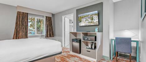 Quarto de hotel com uma cama, uma secretária com cadeira, televisão na parede e uma pequena área de cozinha.