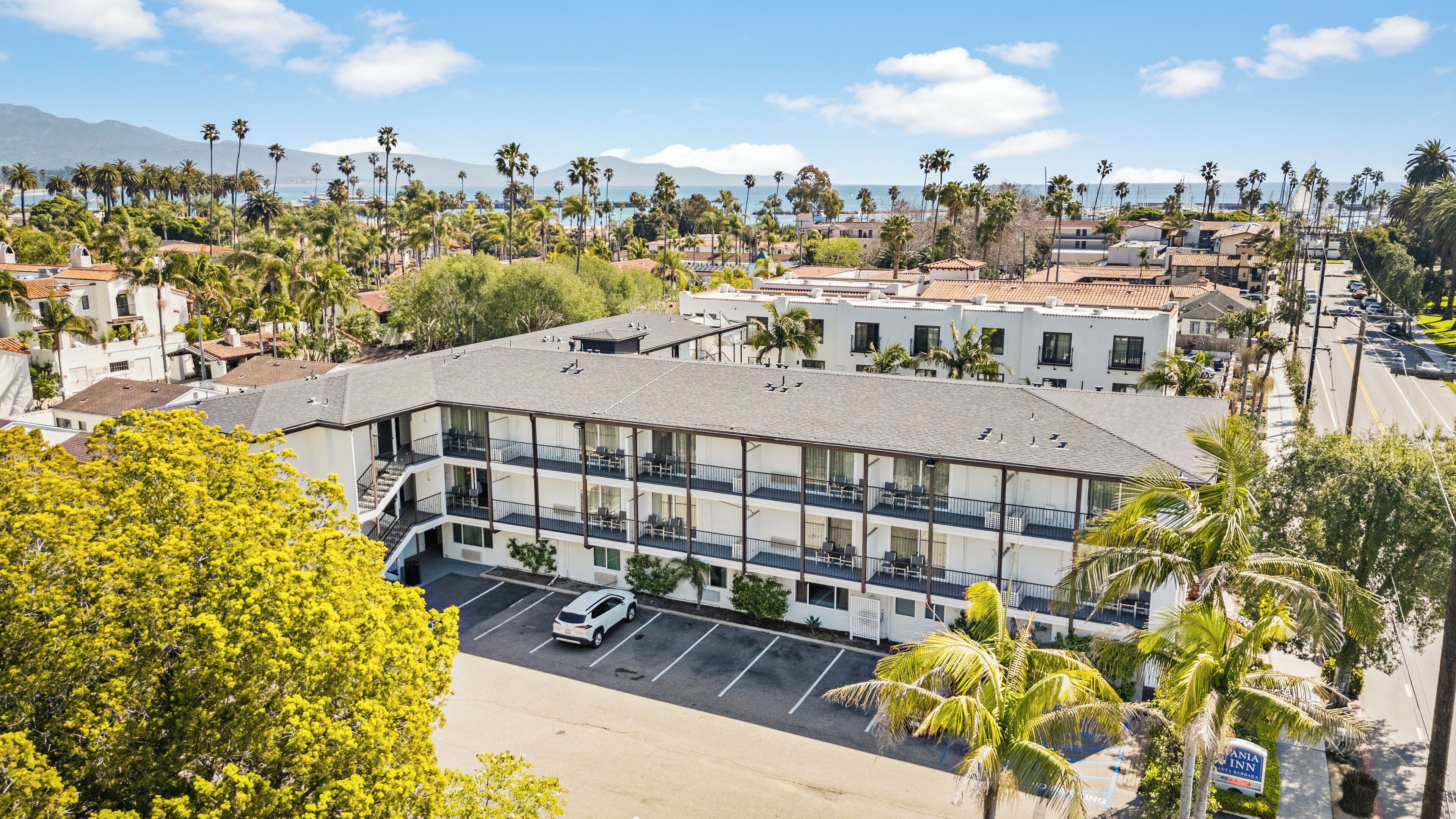 A multi-story hotel with a parking lot, surrounded by palm trees and a view of the ocean.