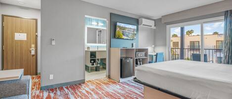 A hotel room with a bed, a desk, a chair, a TV, a mini-fridge, and a bathroom with a shower and toilet.
