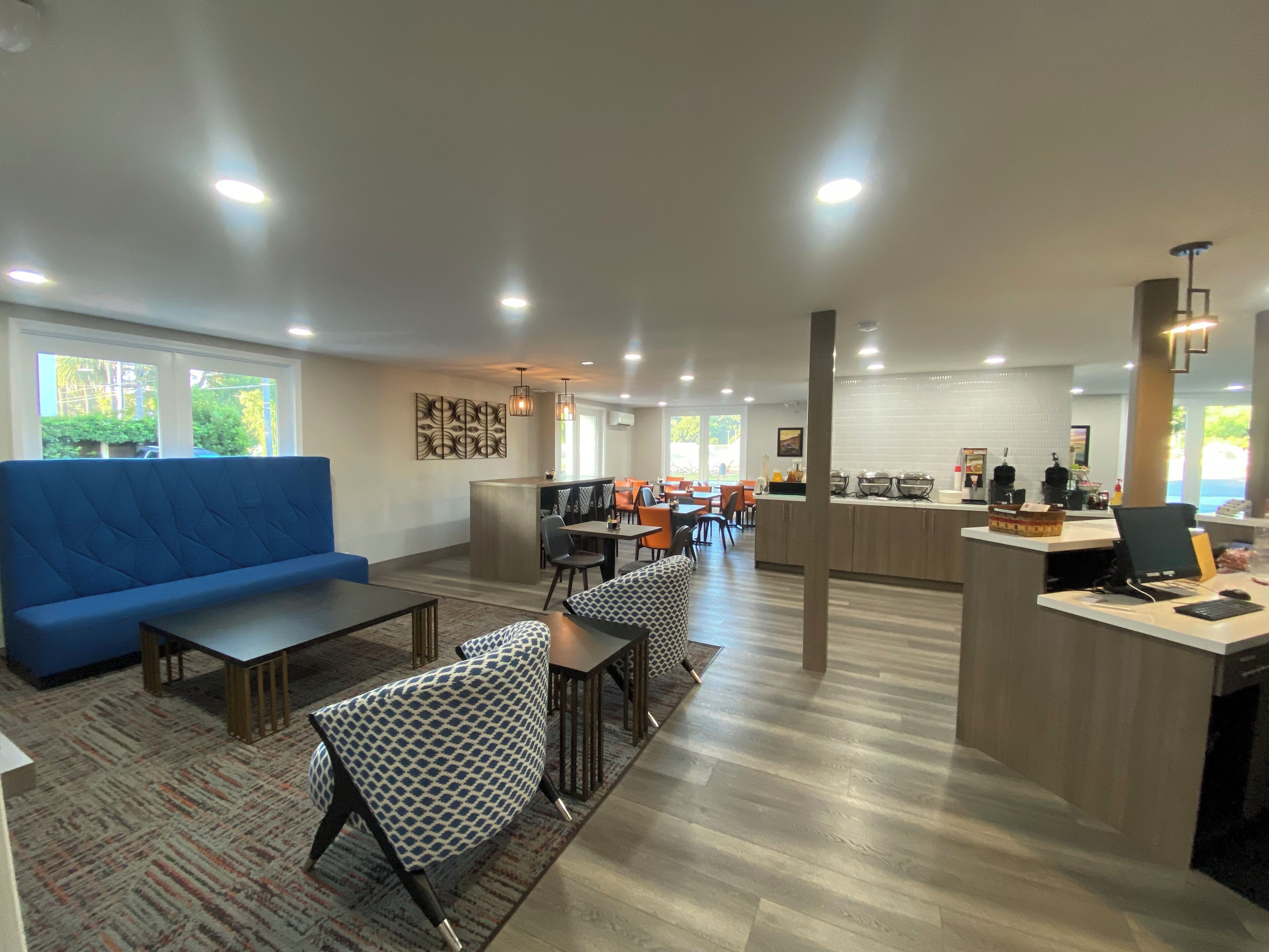 A modern lounge area with a blue sofa, patterned chairs, a central bar, and a dining area with orange chairs.