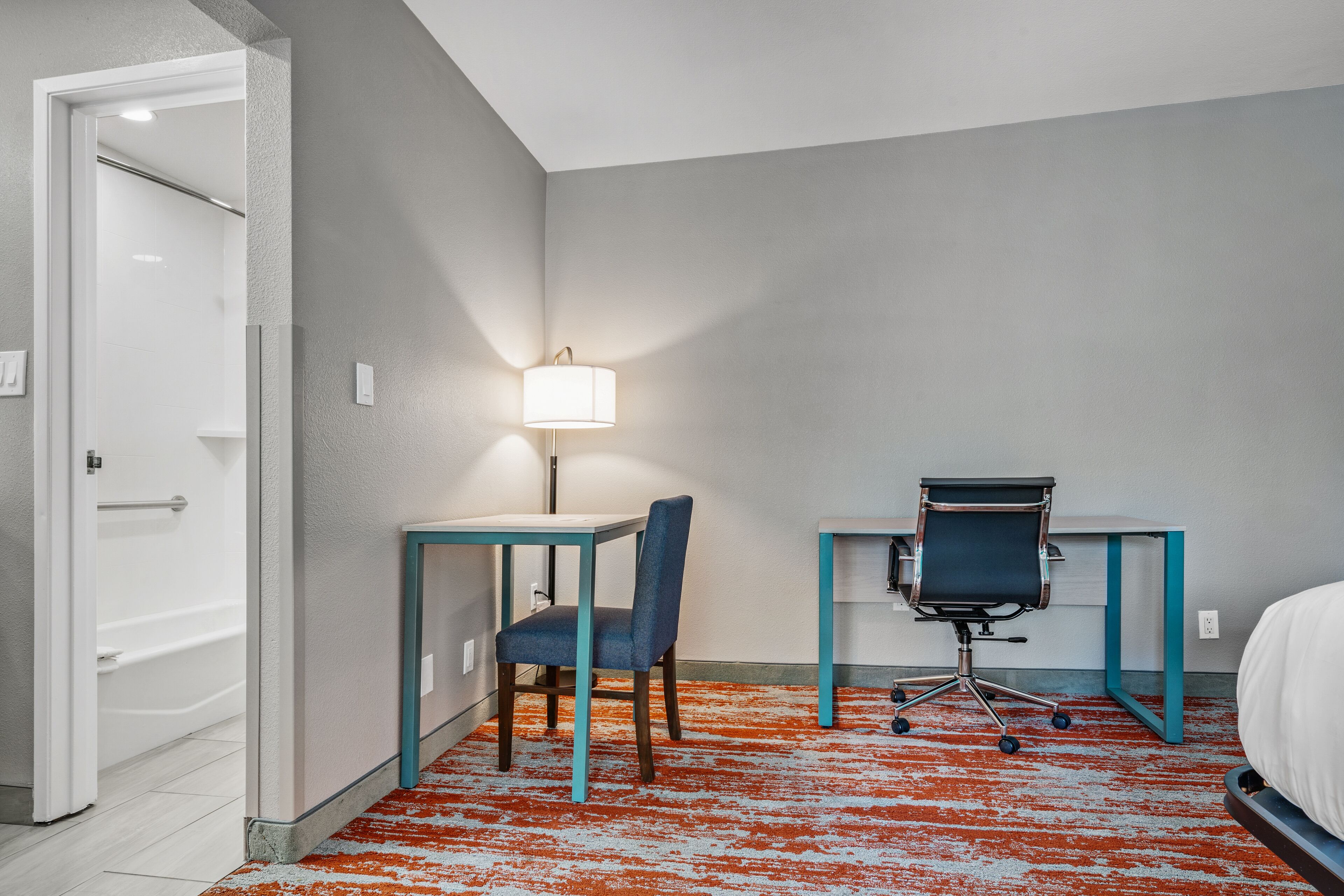 Een hotelkamer met een bed, een bureau met stoel, een lamp en een badkamedeur.