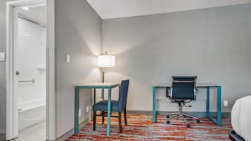 Een hotelkamer met een bed, een bureau met stoel, een lamp en een badkamedeur.