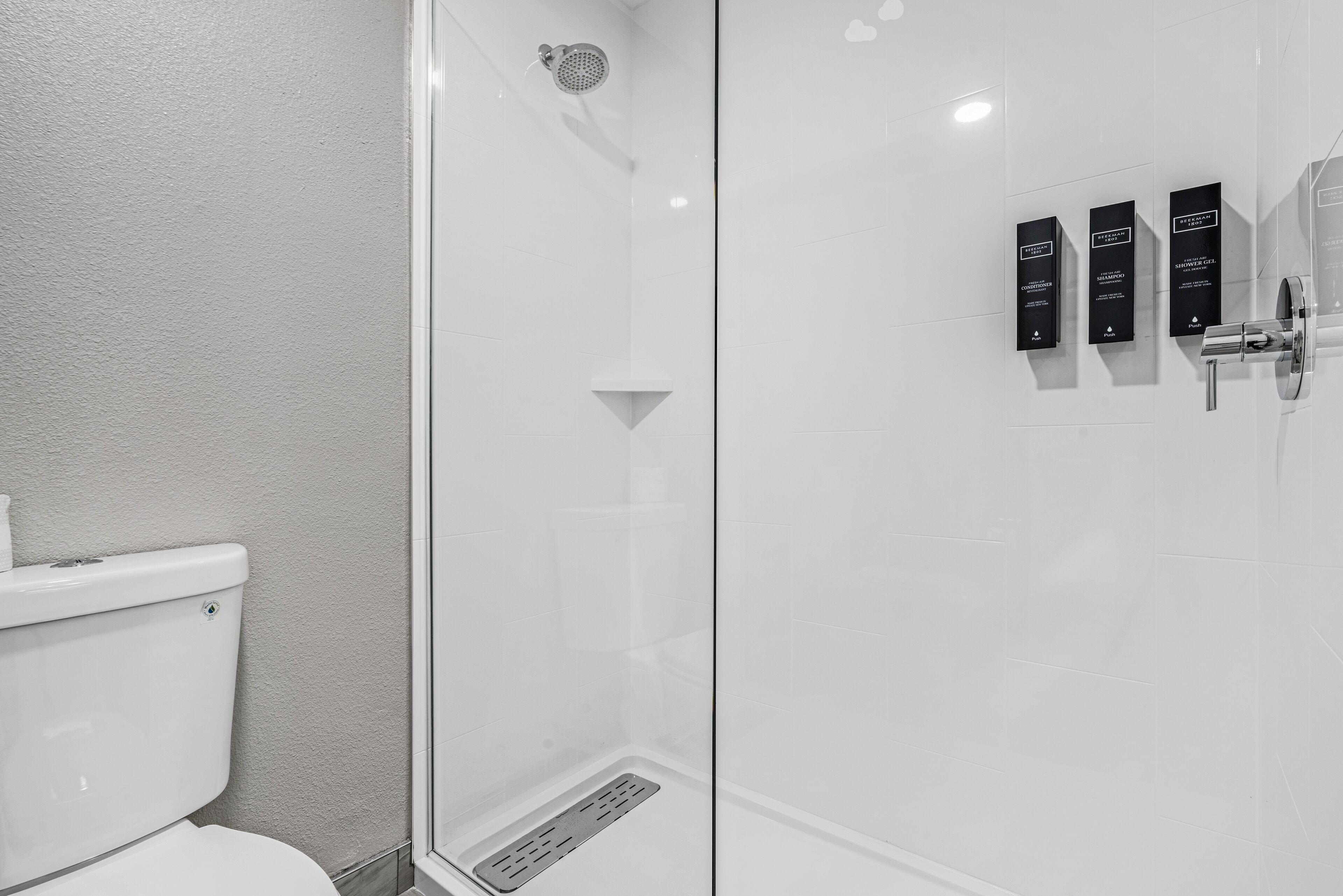 Un baño moderno con ducha acristalada, inodoro y dispensador de jabón en la pared.