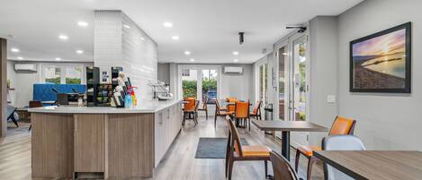 Una cocina moderna con una isla central, comedor con mesas y sillas, y ventanas amplias que ofrecen vistas al exterior.
