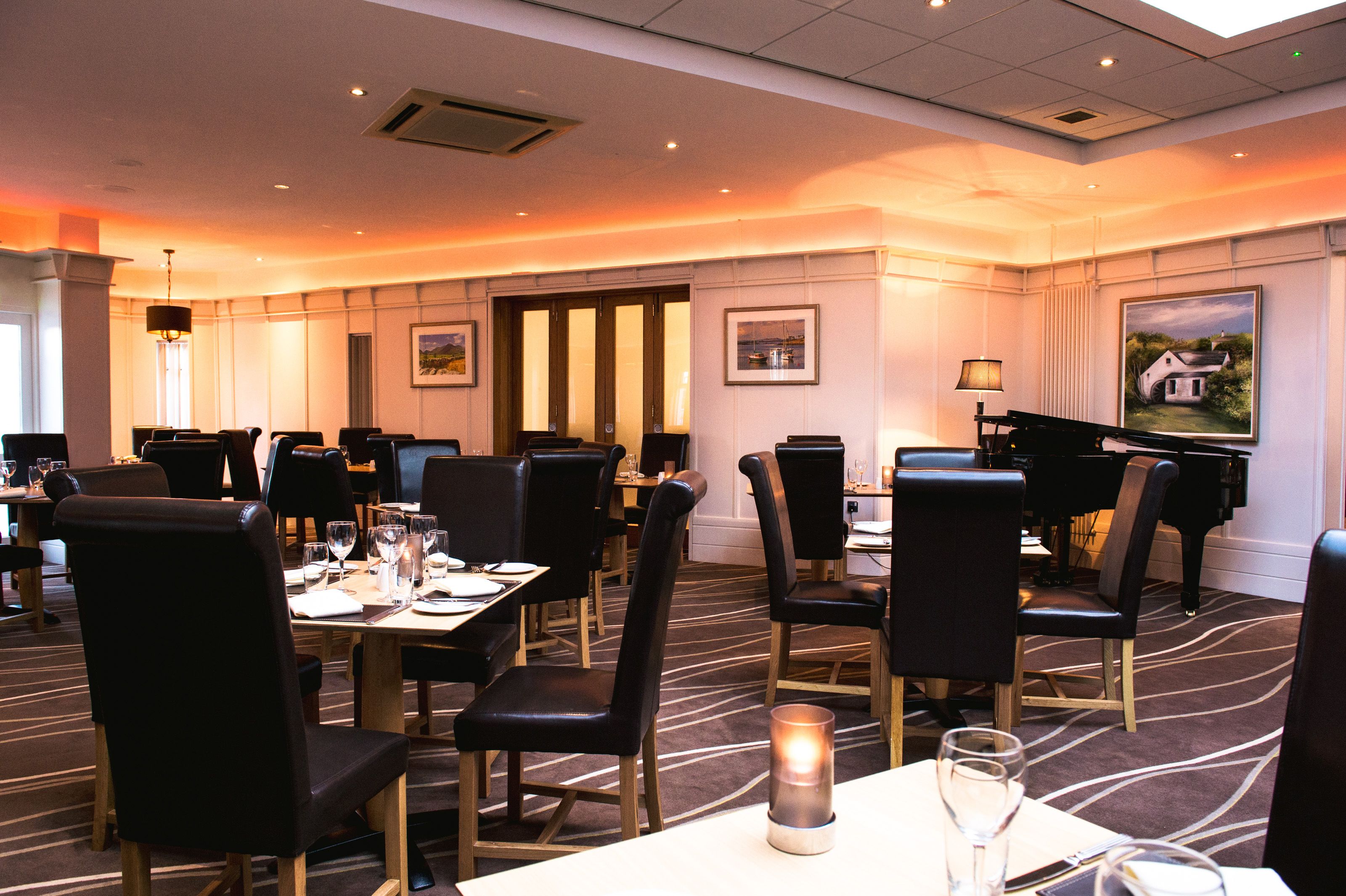 A hotel dining area with multiple tables, chairs, and a grand piano.