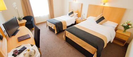 A hotel room with two beds, a desk with a laptop, a chair, a small table with a wine glass, and a potted plant.