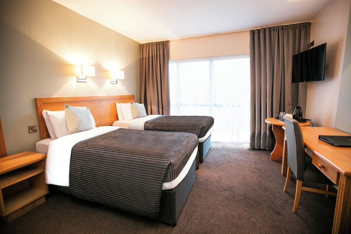 A hotel room with two beds, a desk, a chair, a TV, and a window with curtains.