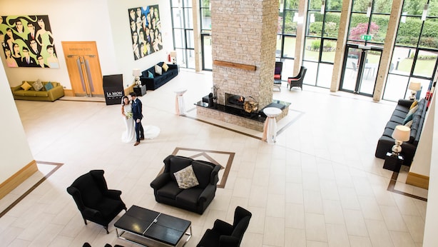 A spacious lobby with a stone fireplace, comfortable seating, and large windows offering views of the outdoors. - La Mon Hotel And Country Club (Newtownards)