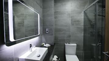 Un baño moderno con un espejo grande, un lavamanos, un inodoro y una ducha con mampara de vidrio.