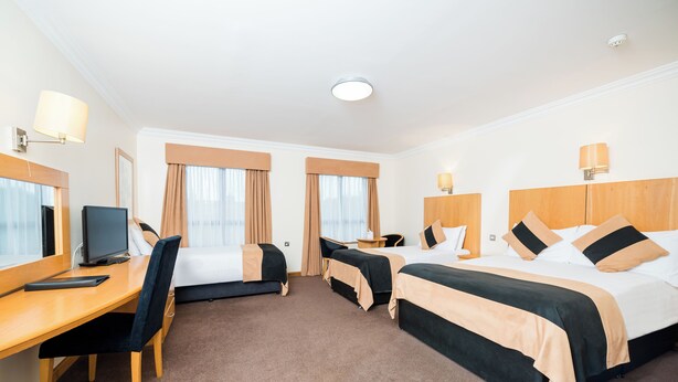 A hotel room with two beds, a desk, a chair, a TV, and a lamp. - La Mon Hotel And Country Club (Newtownards)