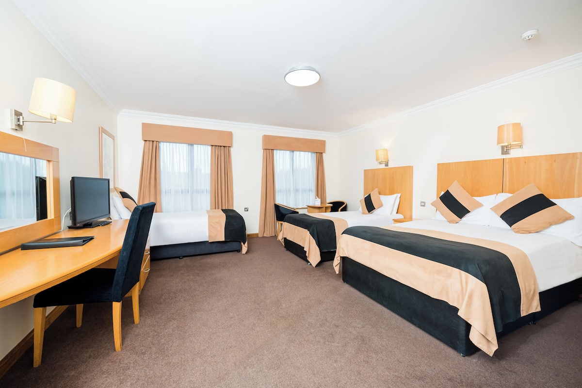 A hotel room with two beds, a desk, a chair, a TV, and a lamp.