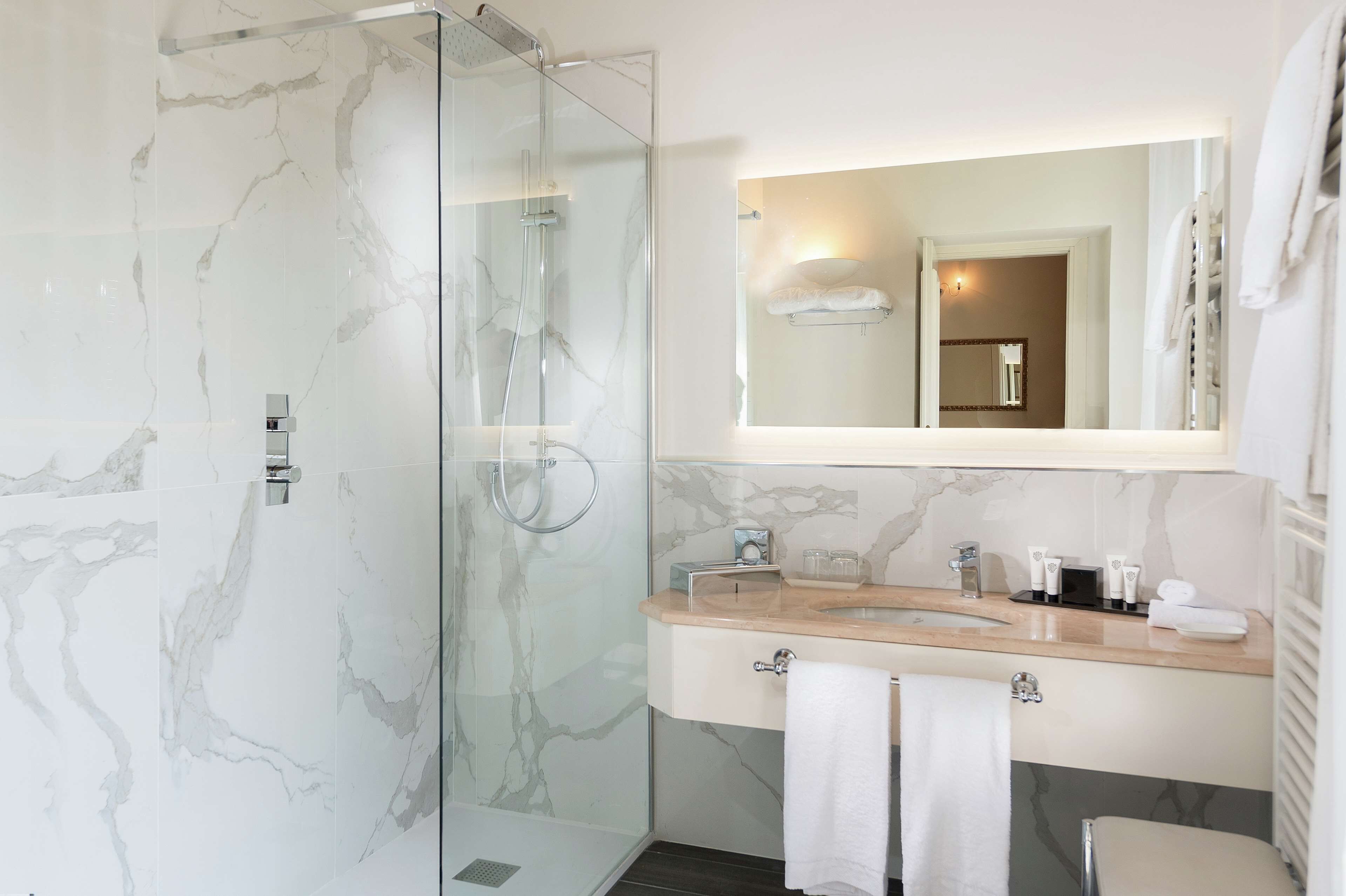 A modern bathroom with a glass-enclosed shower, a marble-tiled wall, a sink with a mirror above, and a towel rack.