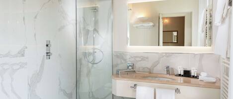 A modern bathroom with a glass-enclosed shower, a marble-tiled wall, a sink with a mirror above, and a towel rack.
