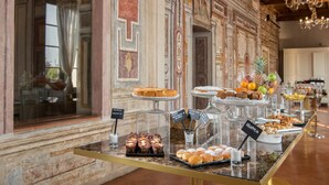 Een buffet met diverse desserts en fruit, met op de achtergrond decoratieve muurornamenten en een kroonluchter.